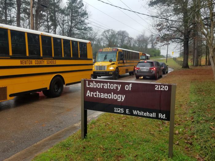 Row of buses lined up next to Laboratory of Archaeology building sign