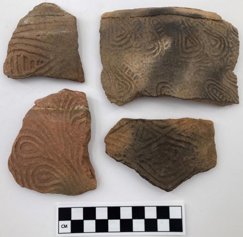 Color photo, 4 Indigenous ceramic fragments of varying sizes with curvilinear motifs, such as teardrops, and one with rectilinear elements.