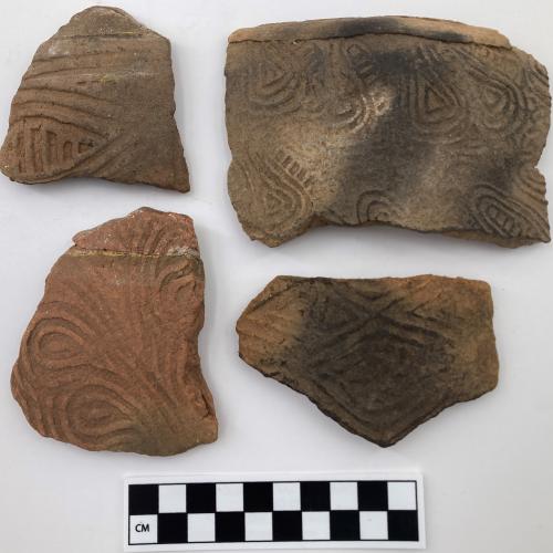 Color photo, 4 Indigenous ceramic fragments of varying sizes with curvilinear motifs, such as teardrops, and one with rectilinear elements.