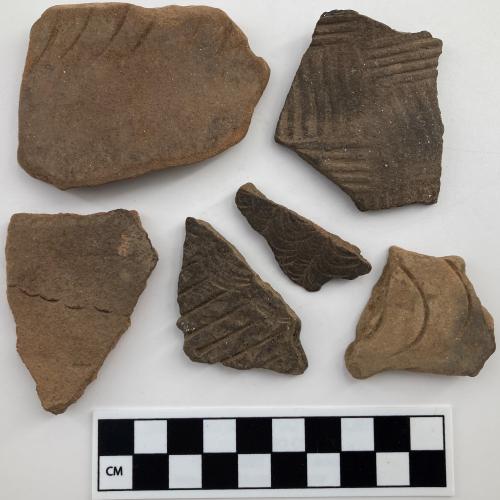 Color photo, 6 Indigenous ceramic fragments of various size and treatment, such as fingernail punctuations, incisions, cross-simple and curvilinear stamps.