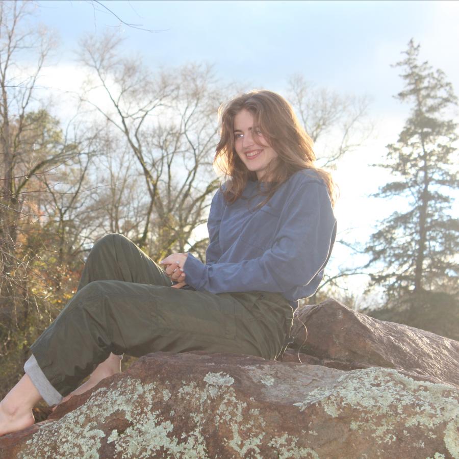 Image of Fiona Ard-Kelly sitting on a large boulder in the forest.