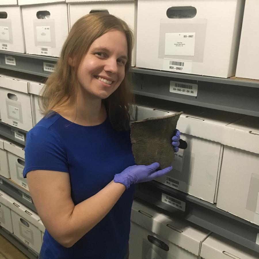 woman holding a sherd with gloved hands in front of a row of curation boxes